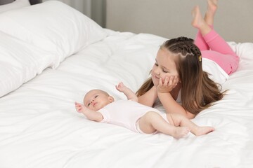 Cute girl and her little sister on bed at home, space for text