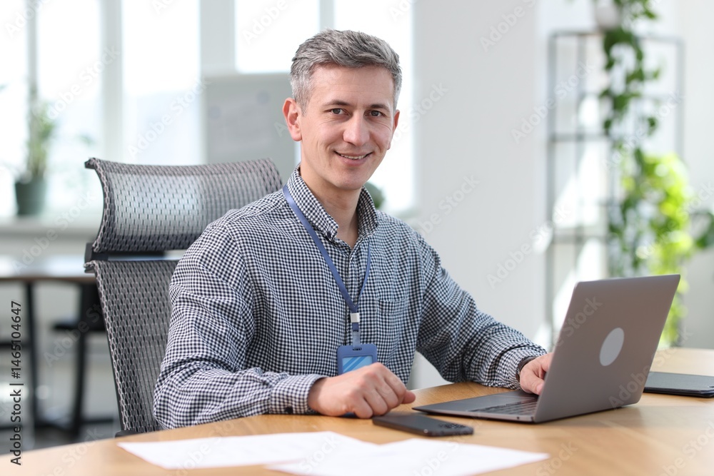 Poster smiling engineer working with laptop at table in office