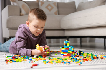 Cute boy playing with building blocks on floor at home. Space for text