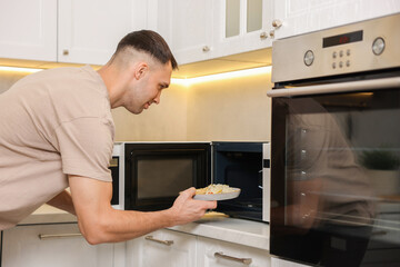Man putting plate with lunch into microwave in kitchen