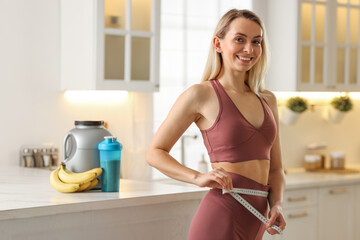 Weight loss. Woman measuring waist with tape in kitchen
