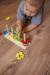 little boy in grey t-shirt playing with educational toy lying on floor. Concept of early child development, learning through play. colorful geometric shapes. close-up of toys