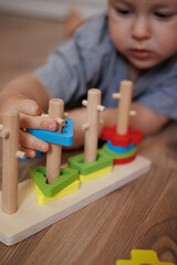 Close-up of a child playing with a wooden educational shape sorter toy. Focus on hands and colorful geometric shapes. Concept of learning through play, fine motor skills, 