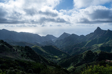 Obraz premium The mountains are covered in trees and the sky is cloudy. The mountains are very tall and the view is breathtaking