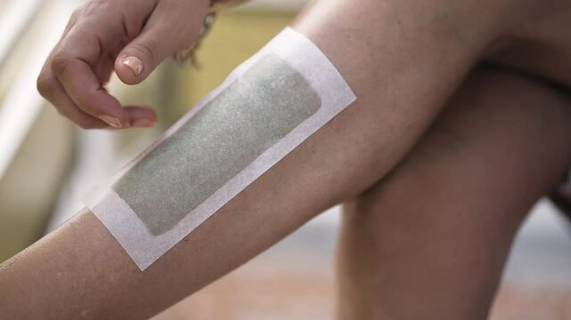 Depilating woman smooth leg with wax strip