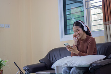 A Hispanic woman relaxes alone on a comfortable couch, listening to wireless music, searching for...