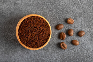 Coffee beans with a bowl of ground coffee on gray background