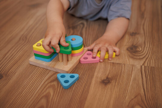 Close-up of child's hands playing with wooden educational toy-sorter. Horizontal photo. Concept of learning through play, fine motor skills and early childhood development