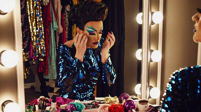 drag queen applying lashes in sparkly outfit under vanity lights, drag queen touching up makeup, drag queen perfecting dramatic glam look. Concept fierce transformation