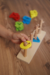 Child’s hand placing shape into wooden Montessori sorting toy. Colorful educational toy for...