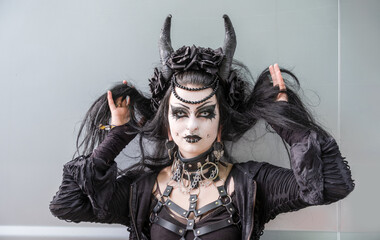 Striking gothic portrait of a woman in black with horns, elaborate makeup, piercings, and leather...