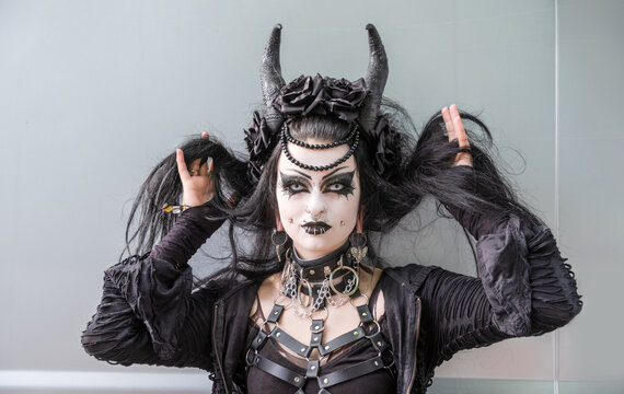 Striking gothic portrait of a woman in black with horns, elaborate makeup, piercings, and leather harness, posing expressively in full costume during an alternative fashion event, WGT, Leipzig