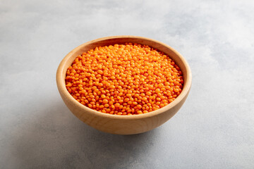 Red lentil grains in a wooden bowl on light blue background. Top view of dried orange lentils inside the bowl.