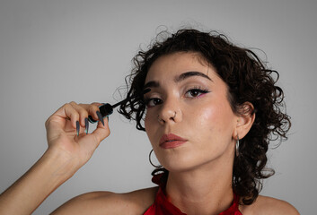 Young curly-haired girl applies eye makeup. Copy space
