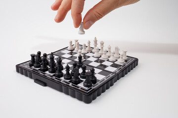 Hand making a move with white chess piece on small plastic chessboard with complete black and white mini magnetic portable chess set. Strategy and competition concept. game for adult and children
