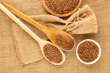 Raw buckwheat with kitchen utensils on jute cloth, top view, macro.