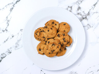 Top view of a plate of freshly baked chocolate chip cookies on a white marble surface