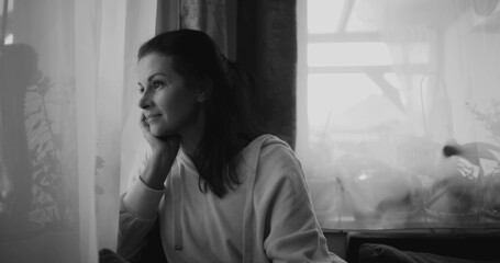 Woman gazing out window, resting chin on hand in thoughtful pose, sitting in peaceful home setting...