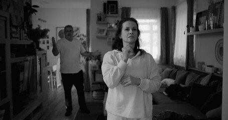 Woman holding her head in frustration during heated argument, while man in background gestures angrily, capturing intense conflict and emotional distress in a couple’s relationship