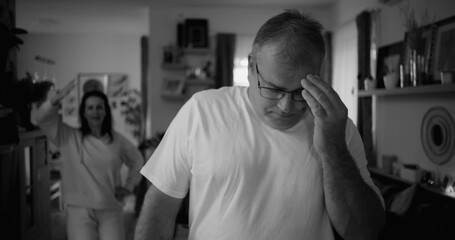 Portrait of man with intense expression during argument, woman in background in living room, focus...
