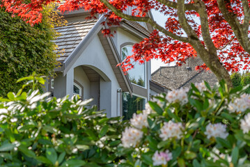 Top of grey stucco luxury house with shingle roof, green trees and nice windows in Spring in...