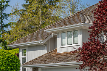 Top of grey stucco luxury house with shingle roof, green trees and nice windows in Spring in Vancouver, Canada, North America. Day time on April 2025.