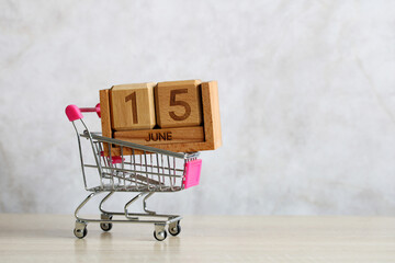 Shopping cart carrying wooden calendar showing june 15th representing online shopping and e-commerce