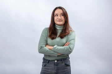 Confident Asian woman in green turtleneck sweater standing with arms crossed and slight smile,...