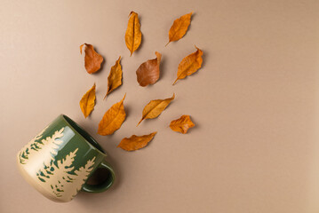 Mug with autumn leaves on beige background. Flat lay, top view.