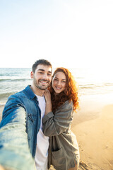 Obraz premium Smiling couple taking selfie on beach at golden hour. Lifestyle. Vacations.