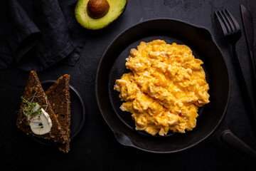 Fresh cooked scrambled eggs in a cast iron skillet on black background, top view