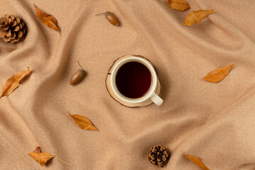 Mug of tea on brown fabric with leaves as concept background. Flat lay, top view.