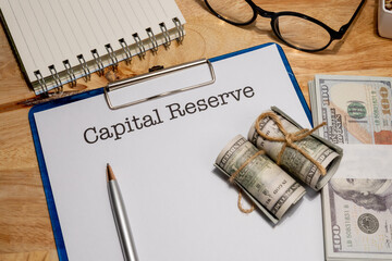 A clipboard holding a capital reserve document is set beside cash, symbolizing retained earnings or...