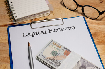 A clipboard holding a capital reserve document is set beside cash, symbolizing retained earnings or...