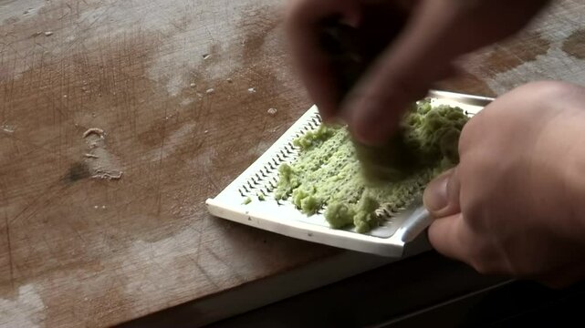 Hands grating fresh wasabi root on metal grater, green paste forming, traditional Japanese culinary preparation, spicy condiment for sushi and sashimi