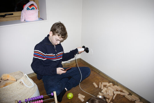 Full length of boy charging smart phone while sitting cross-legged on floor at home