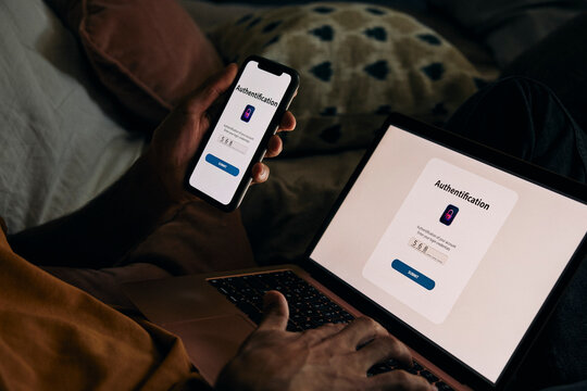 Midsection of man typing password on laptop for authentication through smart phone at home