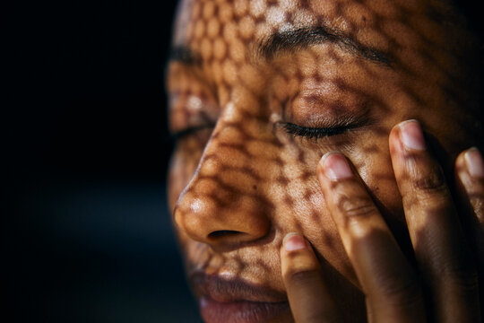 Close-up of sunlight shining on woman with eyes closed touching cheek with hand