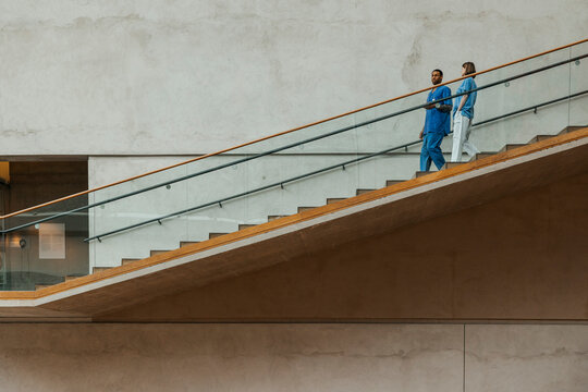 Full length of multiracial male and female nurse talking with each other while moving down steps of hospital building
