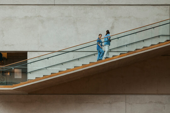 Full length of multiracial female doctors moving up stairs while talking with each other in hospital building
