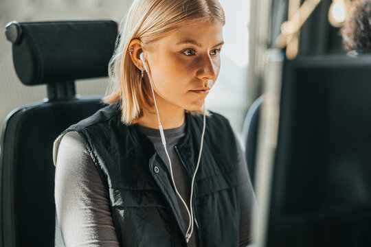 Focused young female entrepreneur wearing headphones working on computer in tech office