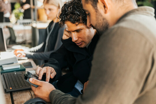 Male software engineers using smart phone while discussing strategies in tech office