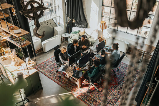 High angle view of multiracial software engineers coding while working sitting at desk in startup office