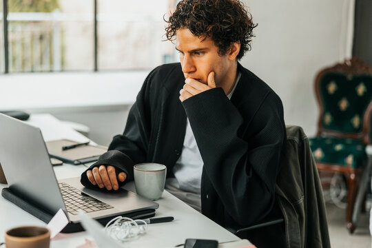 Thoughtful male software engineer working on laptop while sitting at desk in work place