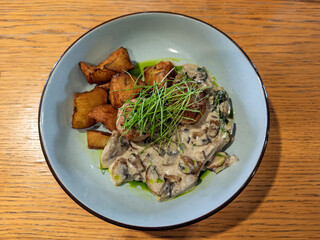 Restaurant Dish: Tender Meat Cutlets in Rich Mushroom Cream with Crispy Potato Wedges, Microgreens.Top View: Meat Medallions, Mushroom Cream Sauce, Potato Wedges and Green Garnish.