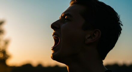 Silhouette of a man screaming against a vibrant sunset sky in profile view