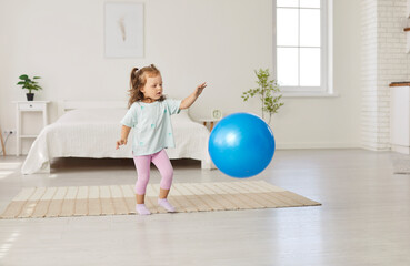 Positive little girl happily playing with a ball at home, enjoying an active leisure activity....