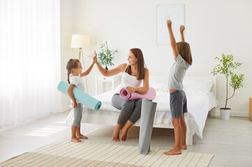 Obraz premium Portrait of happy cheerful sporty family of mother with kids standing in bedroom holding yoga mat in hands going to do sport morning exercises at home. Workout and healthy lifestyle concept.