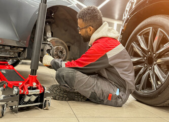 An African-American tire fitter with a wrench in his hands while working. The tire fitter removes...