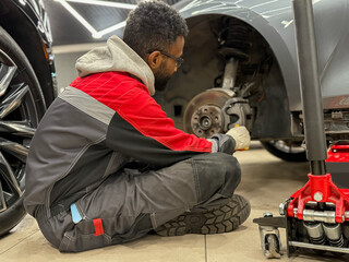 An African-American tire fitter with a wrench in his hands while working. The tire fitter removes...